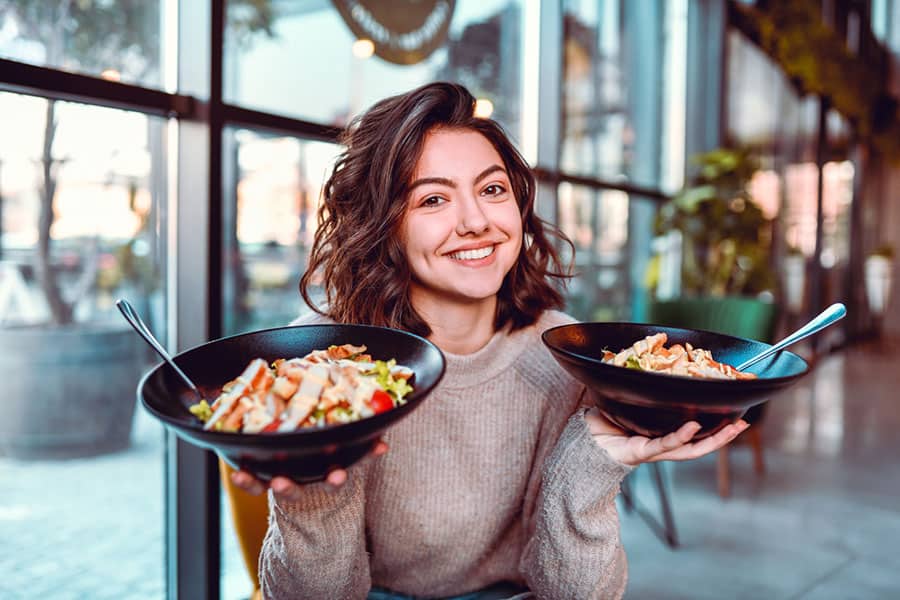 Girl happily posing with 2 healthy meal bowls