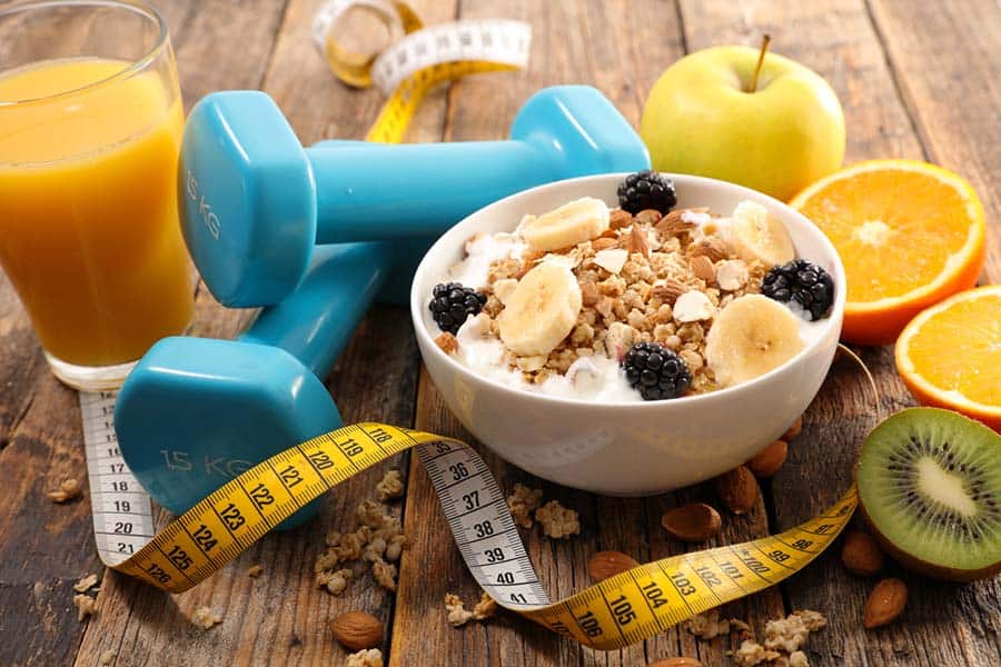 A pair of dumbbells and measuring tape lying next to a healthy breakfast meal