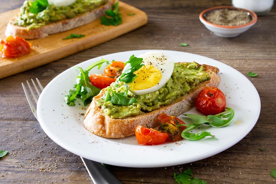 Healthy breakfast plate with low-calorie bread, boiled eggs, guacamole, and tomatoes