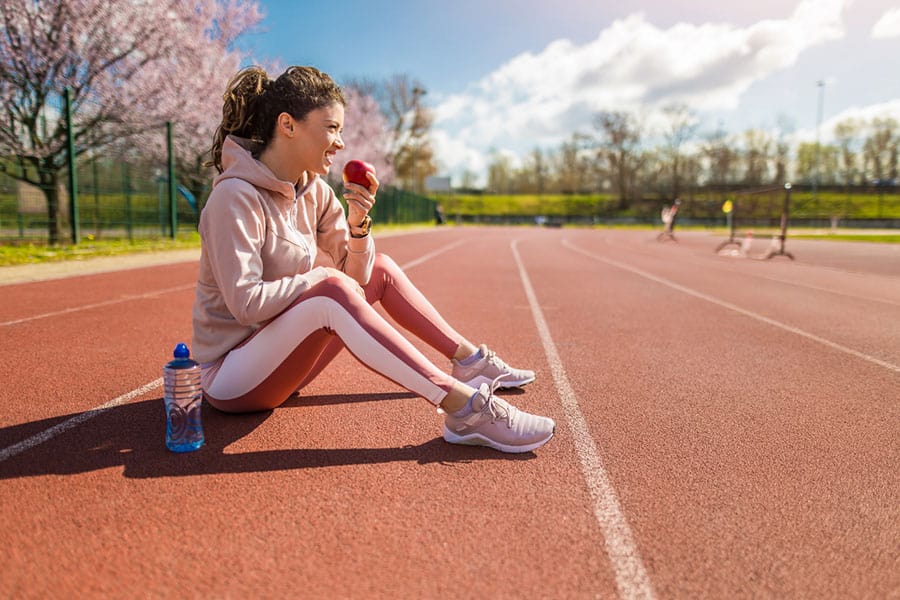 A girl sitting on the runner's track and eating fruit after a sprint