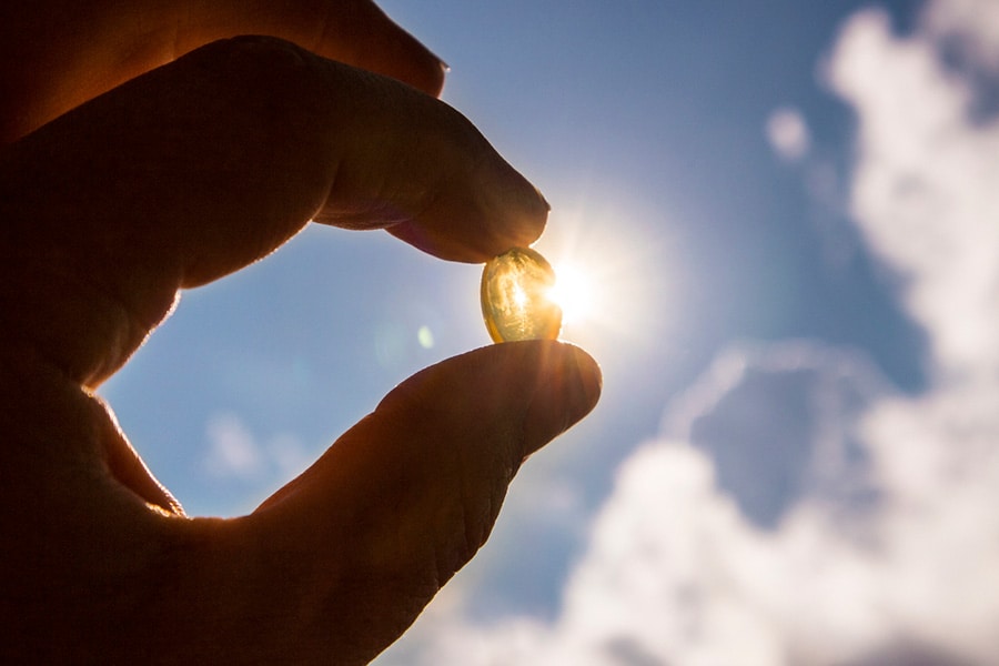 Yellow soft shell vitamin D capsule held up against a sunny sky
