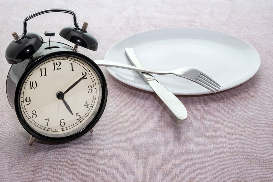 The fork and spoon placed in the plate with an alarm clock by the side.