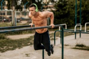 Young fitness muscular man doing dips on parallel bars outdoors and enjoying the music