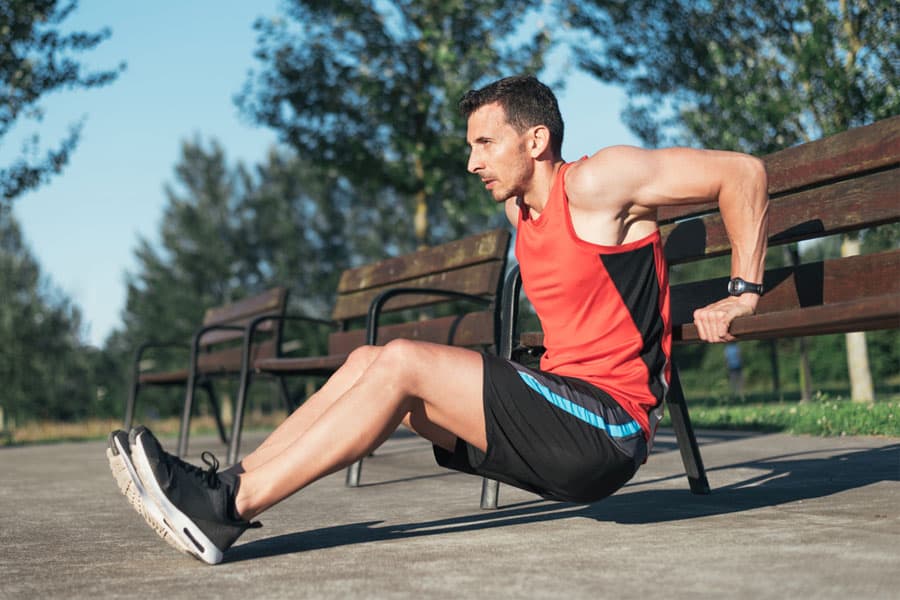 Muscular man doing bench triceps dips during outdoor cross training workout.