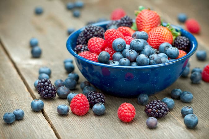 A blue bowl of mixed berries filled with strawberries, raspberries, blueberries and mulberries.