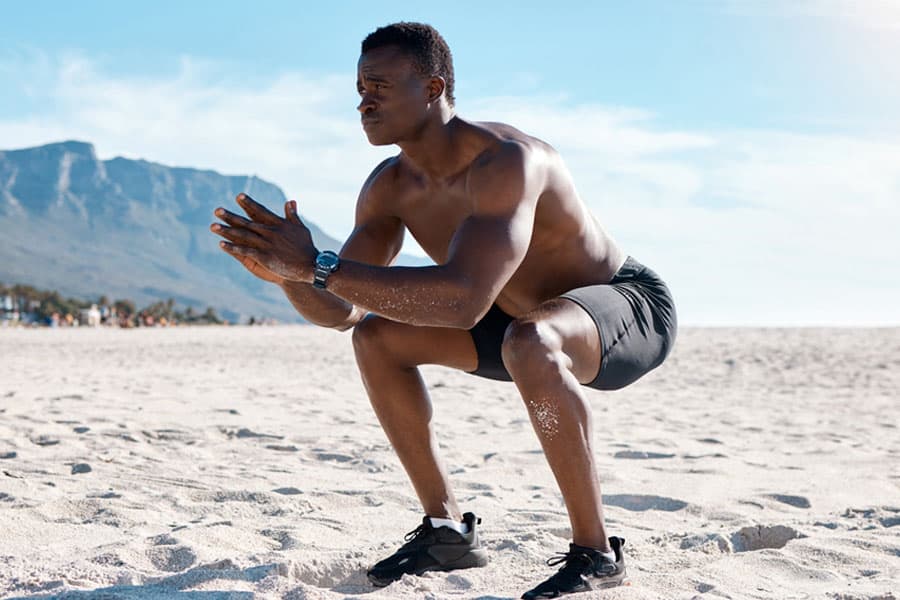 A fit man performing squats on the beach.