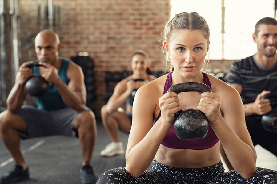A close up of a gym enthusiast working out with a kettlebell at gym in a group