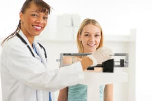 a physician is measuring weight of a teenager with a measuring scale/machine