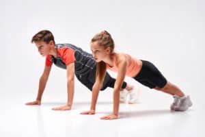 A teenage boy and girl engaged in sport, looking away while doing push-ups.