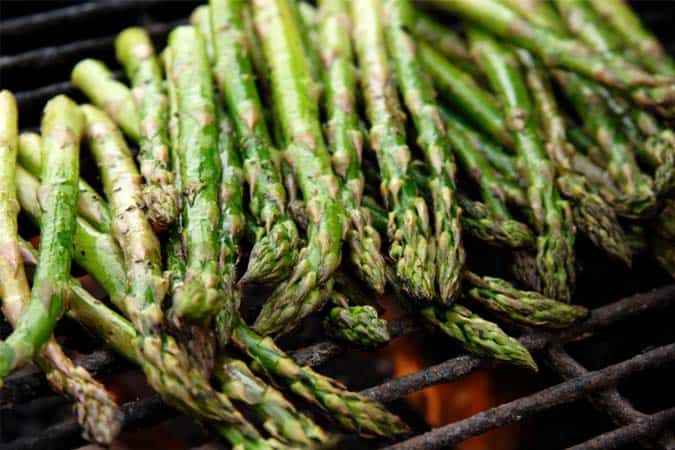 Asparagus stalks are getting cooked on an open fire grill.