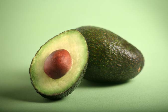 One sliced and one whole avocado on a green surface.