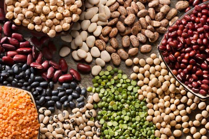 Different types of lentils including chickpeas, kidney beans, red kidney beans, black kidney beans, and yellow and green lentils, are lying on a table.