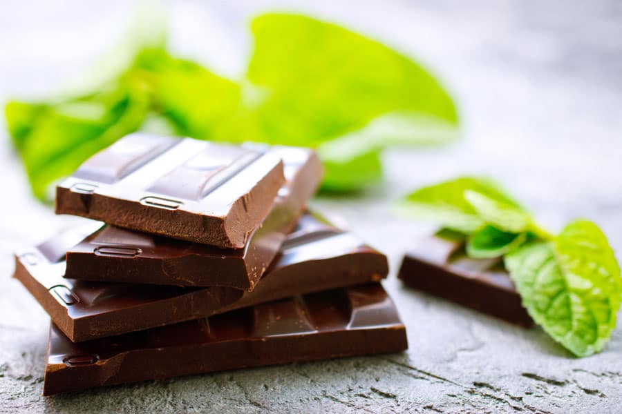 A close up of vegan chocolate placed on a surface with the leaves of mint nearby.