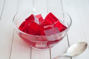 A bowl of jelly is placed on a table with a spoon placed next to it.
