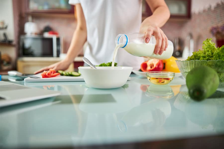 A female is pouring milk in the bowl placed on kitchen shelf