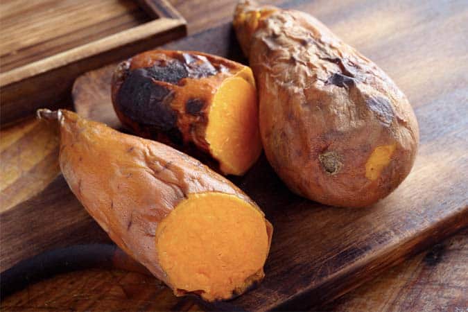 Cooked sweet potatoes are lying on a wooden table.