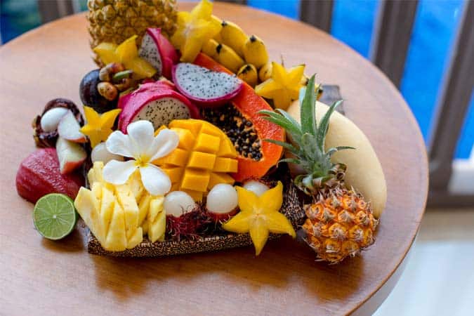 A tray of tropical fruits including mangoes, pineapples, bananas, mangosteen, rambutan, dragon fruit, star fruit, and lemon.