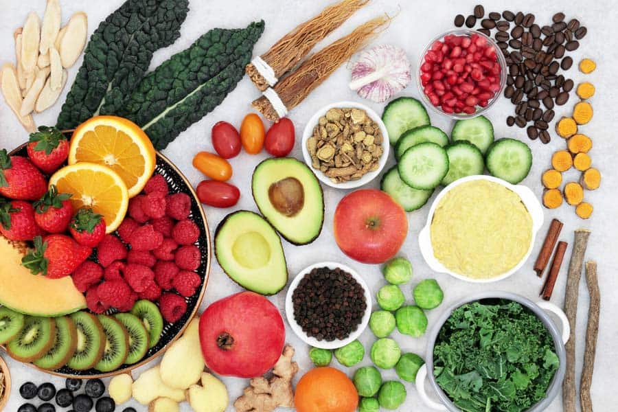 Vegan anti-inflammatory diet foods like strawberry, avocado, apple, pomegranate, cucumber and many more are on a table.