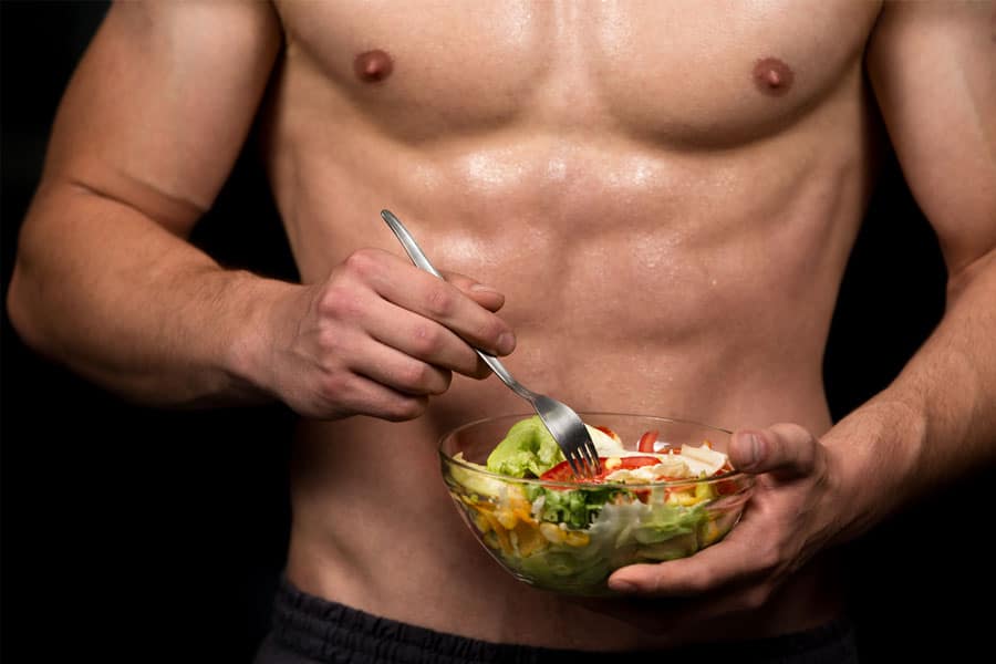 A body builder is seen eating a bowl full of vegetables and other vegan ingredients.