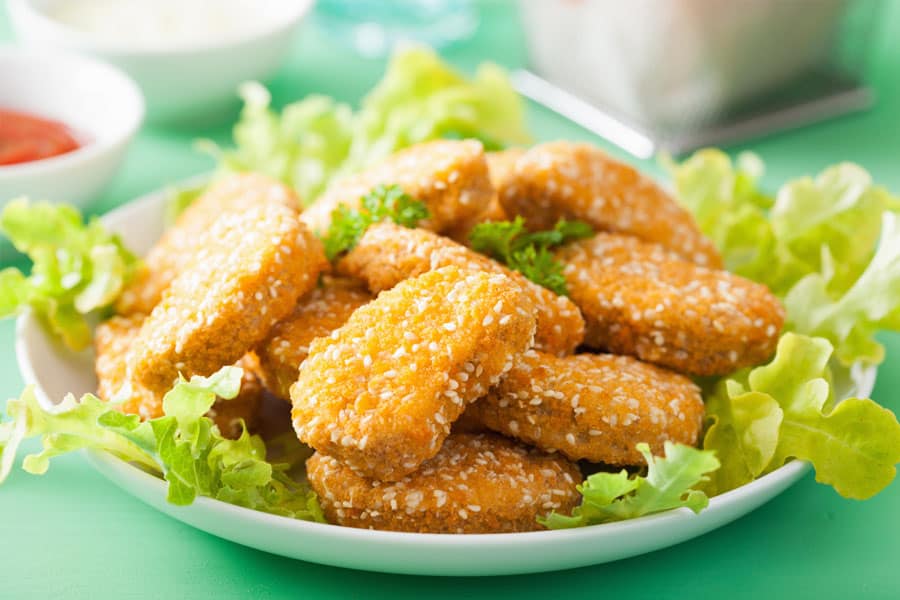 A plate with vegan chicken nuggets placed on the lettuce can be seen on a table. These nuggets look like chicken nuggets.