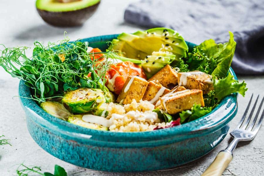 A close-up of a vegan bowl filled with tofu, lettuce, and other veggies.