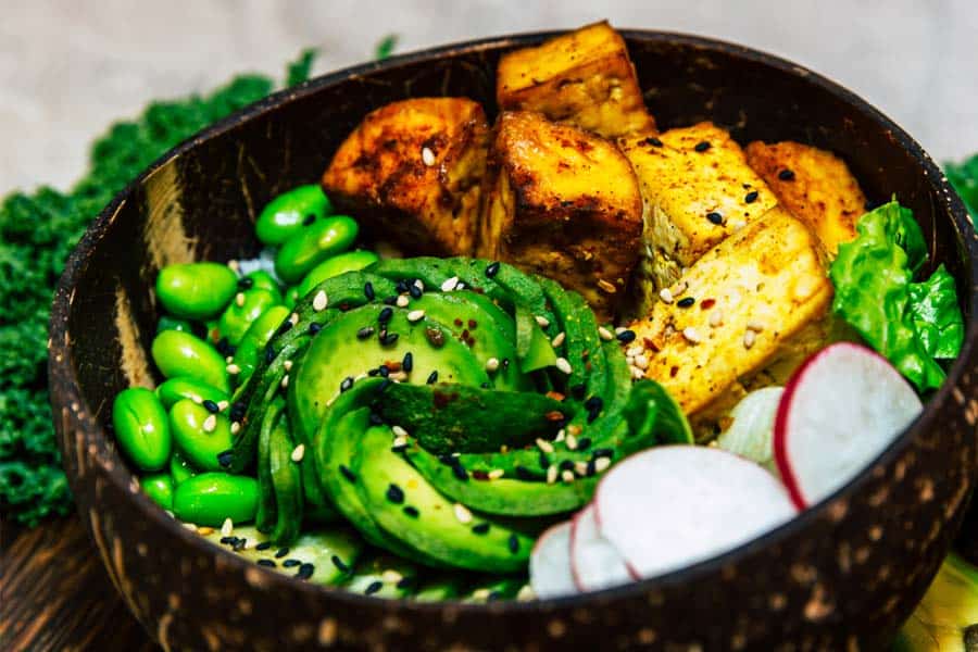 A bowl full of vegan items like tofu, avocado, sesame seeds, cilantro and more.