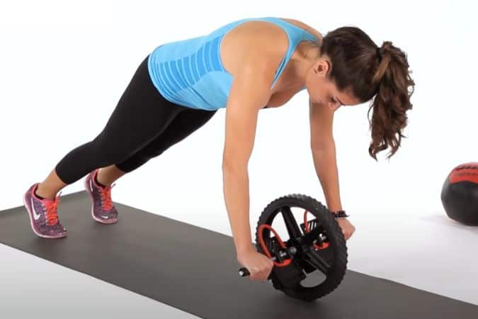 A woman performing the abs wheel rollout exercise on a mat.