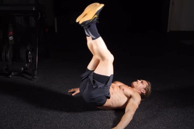 A man performs reverse crunches at a gym.