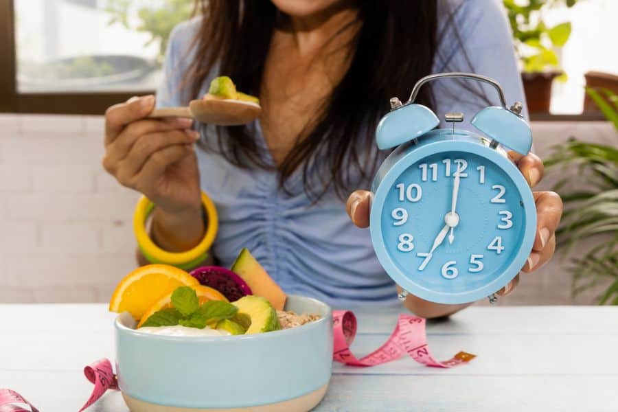A female is holding an alarm clock and having her food - How to get into ketosis in 24 hours